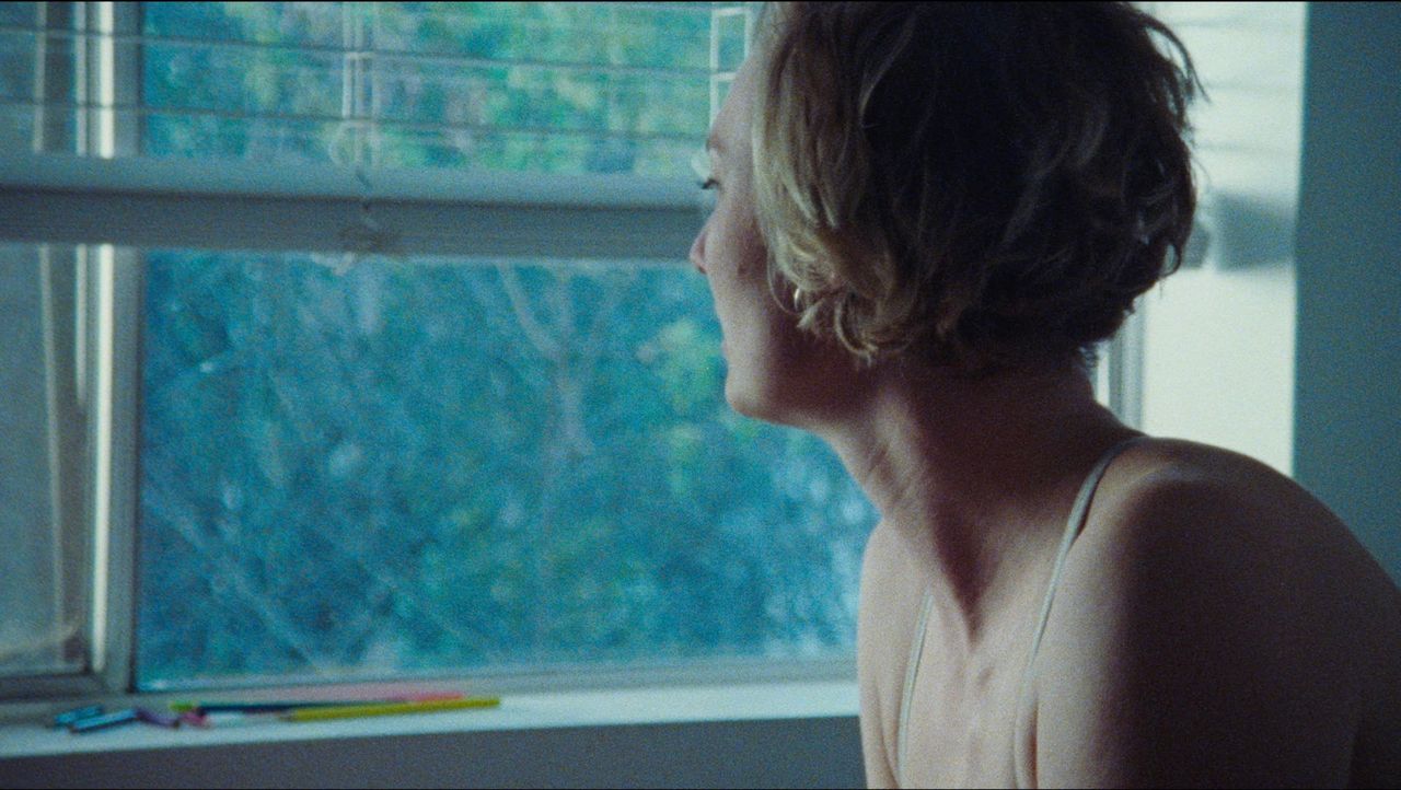 Woman in white top gazing out window with colorful pencils on sill