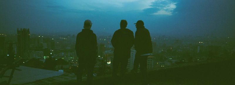 Three silhouetted figures overlook a city skyline at dusk.