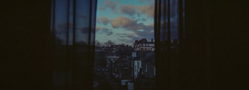 Cinematic dusk view of London residential rooftops and clouds through a window.