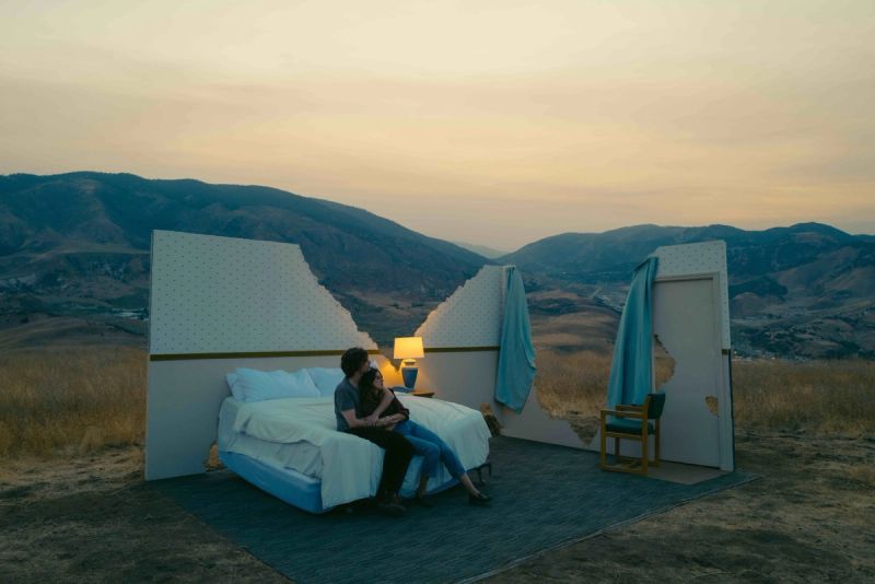 Couple embracing on a bed in an open-air bedroom set against mountainous landscape at dusk