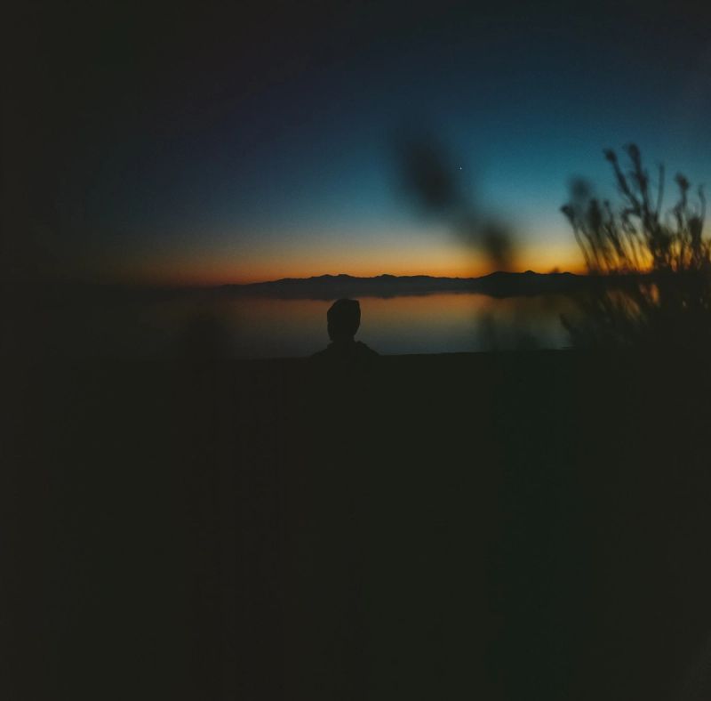 Silhouette of a person overlooking Antelope Island at sunset with mountains in the distance.