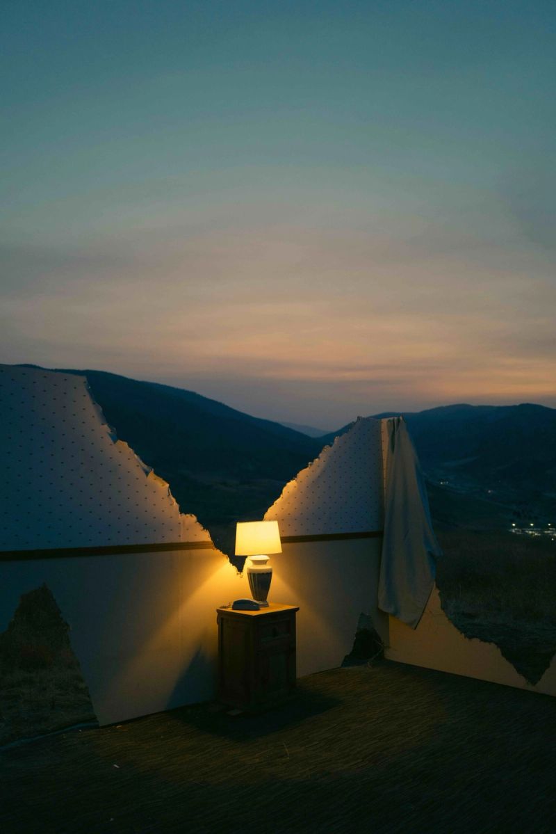 Lamp on nightstand in broken wall overlooking mountain valley at dusk