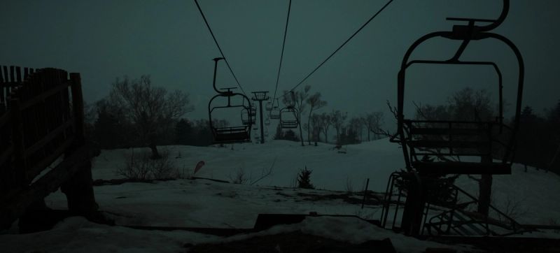 Silhouetted ski lift chairs against a dark, snowy mountain landscape at dusk.