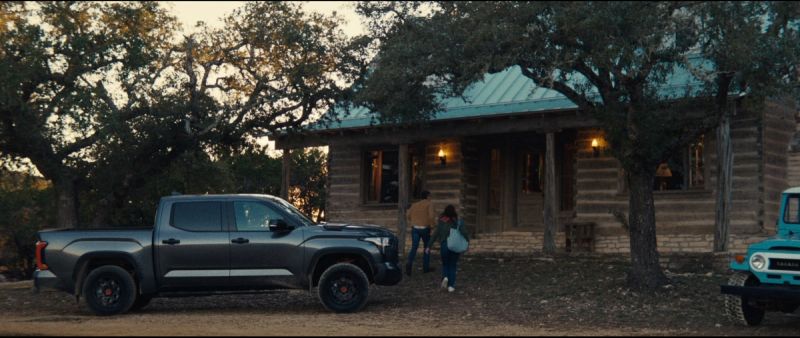 A grey Toyota Tundra truck parked in front of a log cabin with people walking to the entrance.