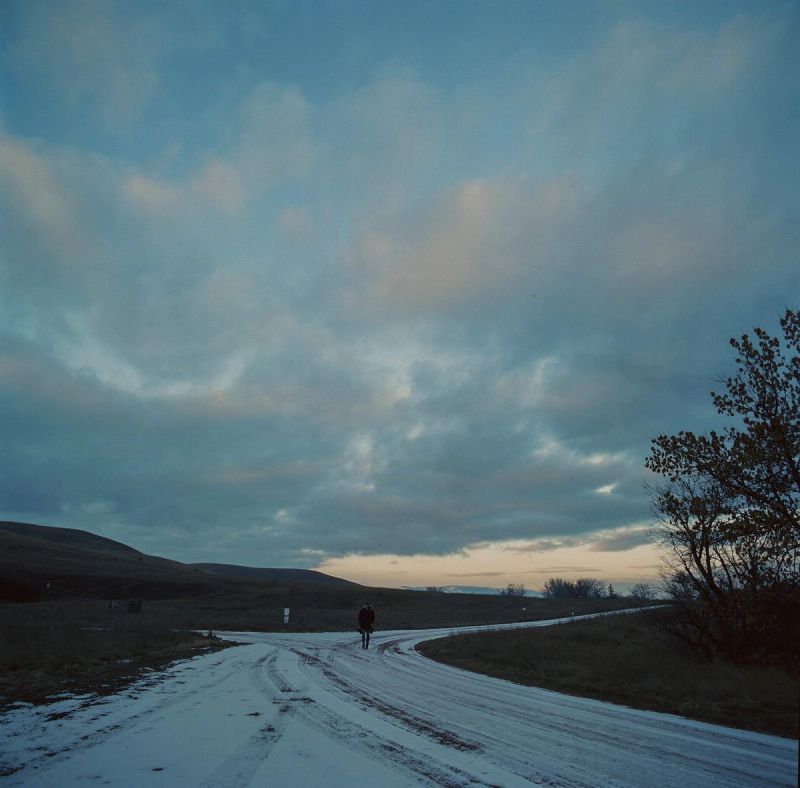 Cyclist on snowy rural road under dramatic cloudy sky