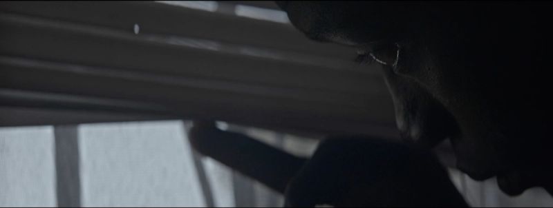 Close-up profile of a person's face in shadow, looking down at a window frame.