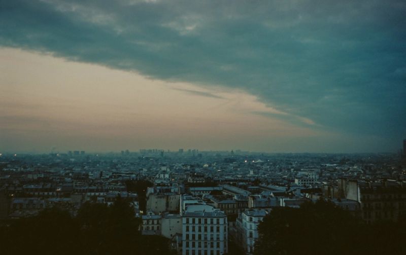 Dramatic twilight cityscape of Paris with moody clouds and film photography aesthetic.