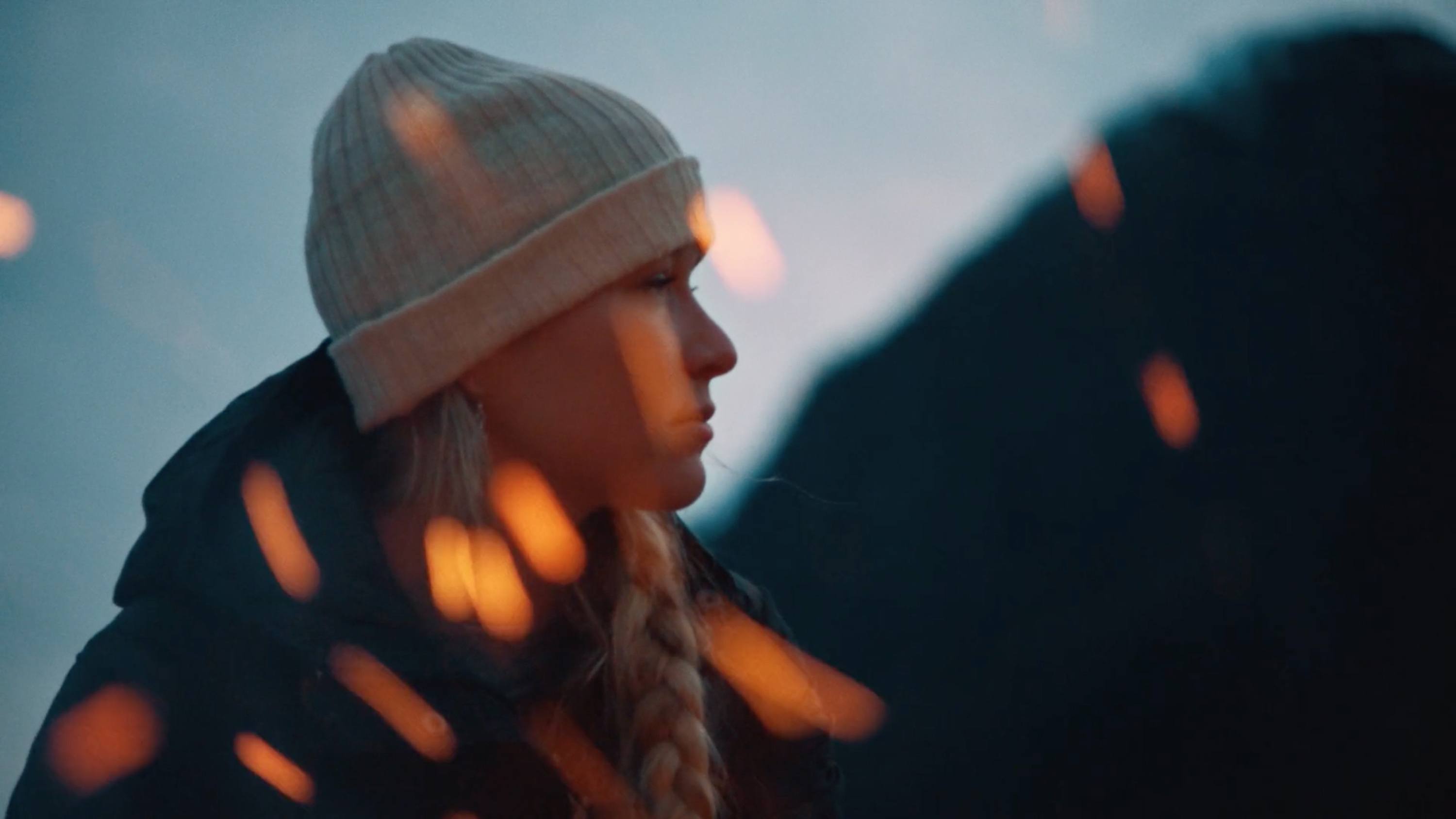 Profile of woman in knit beanie with bokeh lights and mountain silhouette at dusk.