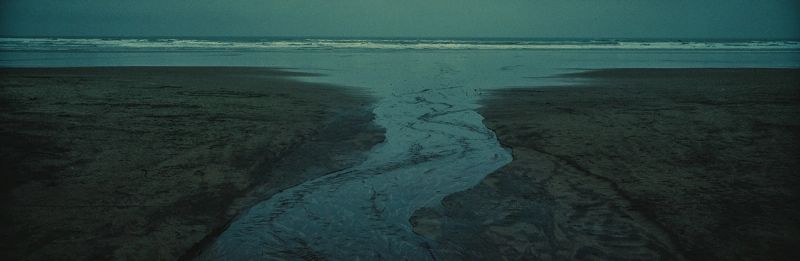 A moody film photograph capturing a stream cutting through wet sand on an Oregon beach.