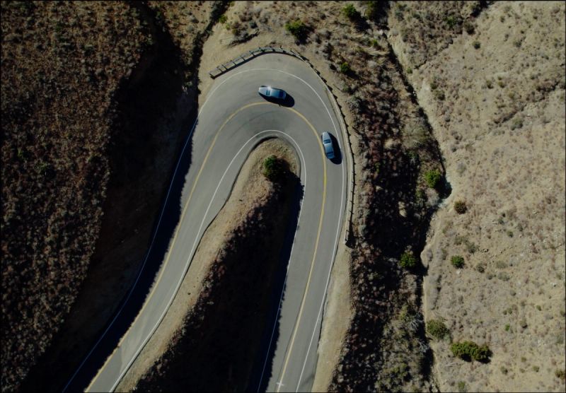 Aerial view of two cars driving on a winding road through dry terrain.