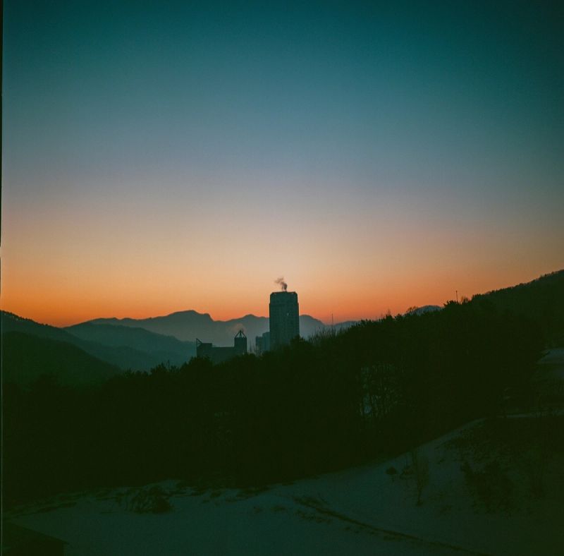 Silhouette of a building and snowy mountains against a blue and orange sunset sky in South Korea.