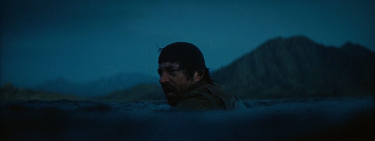 Man wading in dark water with mountain backdrop at dusk