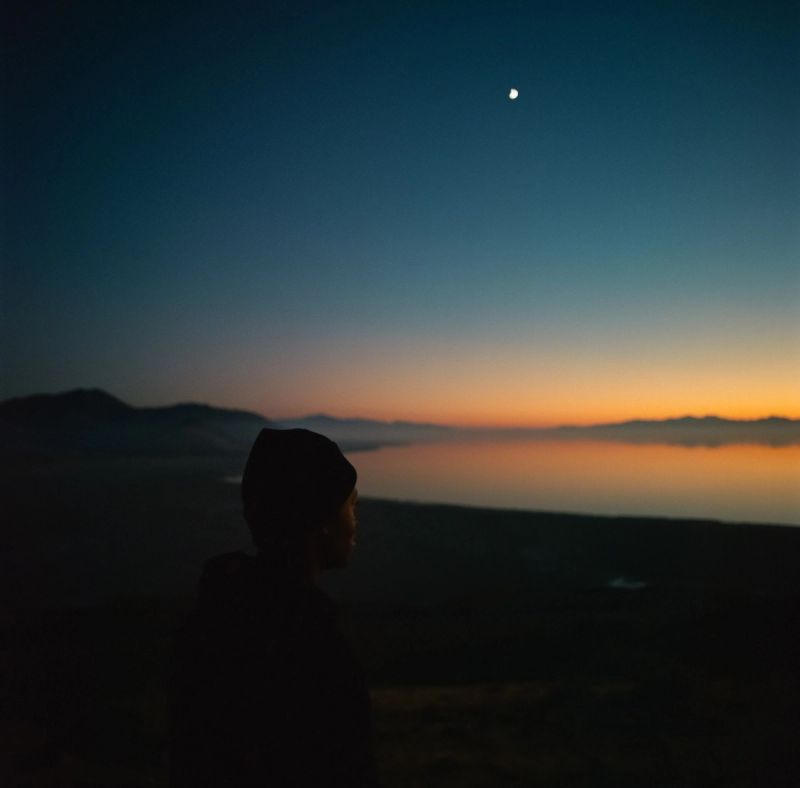 Silhouette of person watching moon over mountain lake at twilight