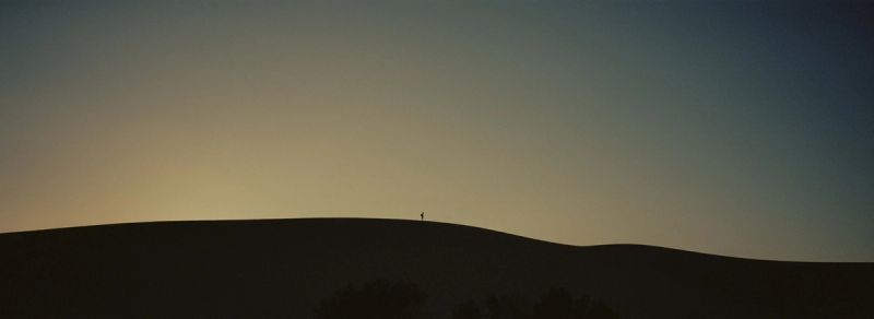 Silhouette of a lone figure standing atop a desert ridge against a gradient dusk sky.
