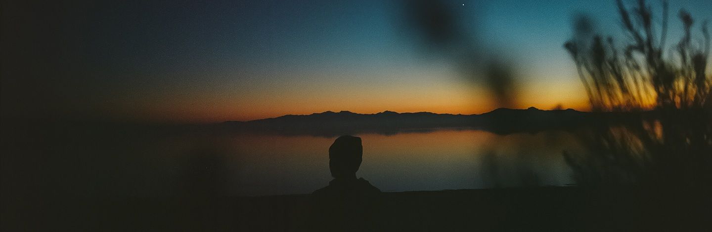 Silhouette of a person watching the sunrise over mountains and water