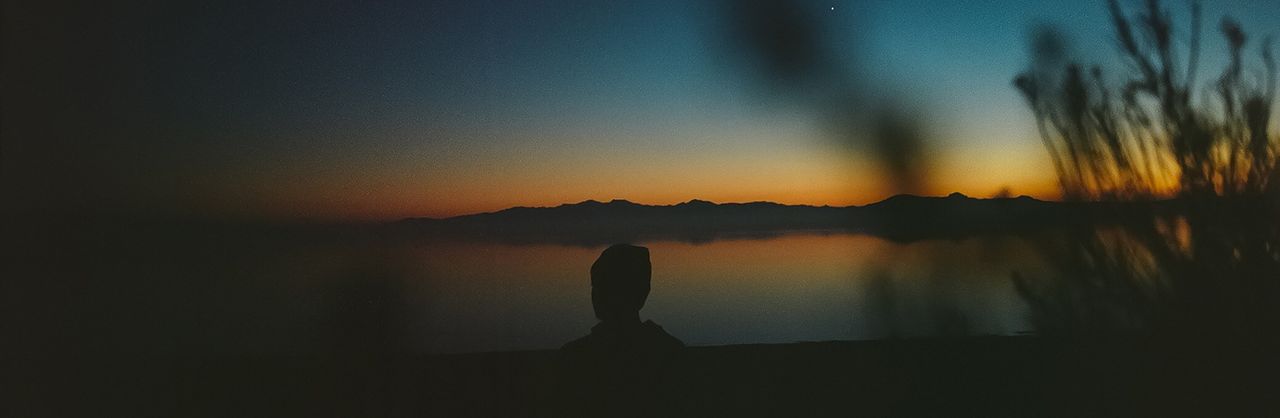 Silhouette of a person watching the sunrise over mountains and water