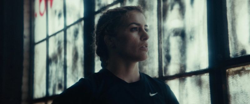 Olympic wrestler Helen Maroulis looking out a grime-streaked industrial window wearing a black Nike shirt.