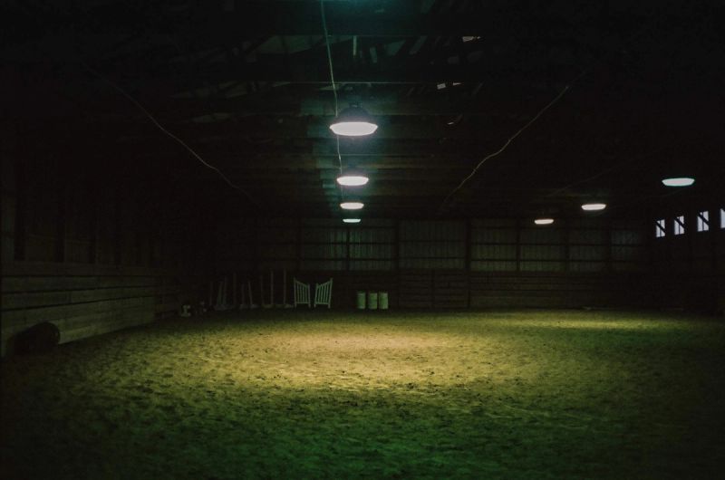 Dark indoor arena with dirt floor and hanging lights, film still from Yellowtail.