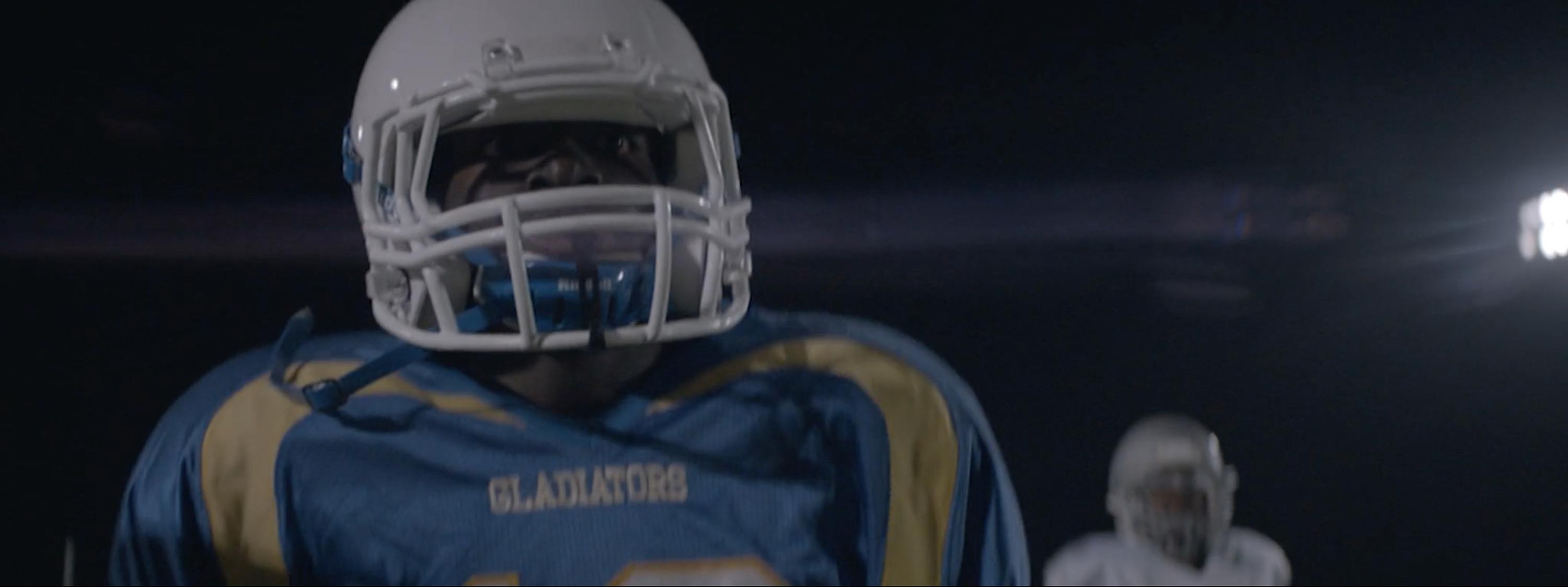 Football player in blue and gold Gladiator uniform under stadium lights at night