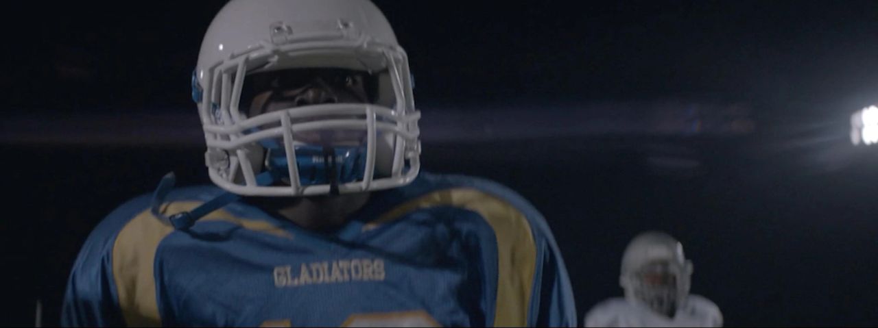 Football player in blue and gold Gladiator uniform under stadium lights at night