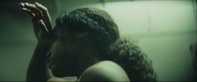 Profile shot of female athlete with curly hair, hand raised near face in moody lighting.