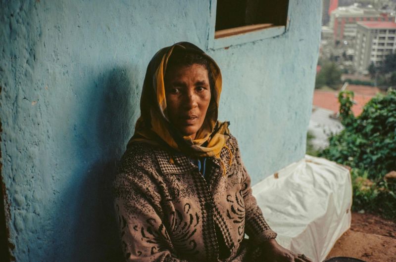 Portrait of a woman in patterned sweater and yellow scarf against blue wall.