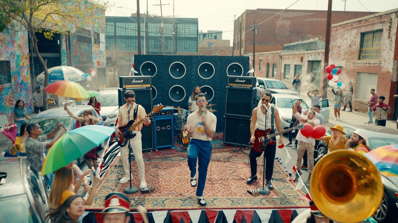 Jonas Brothers performing on a colorful street stage with crowd and balloons in Los Angeles