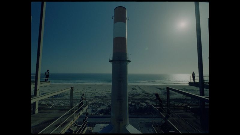 Tall striped smokestack on beach with ocean and sun in background