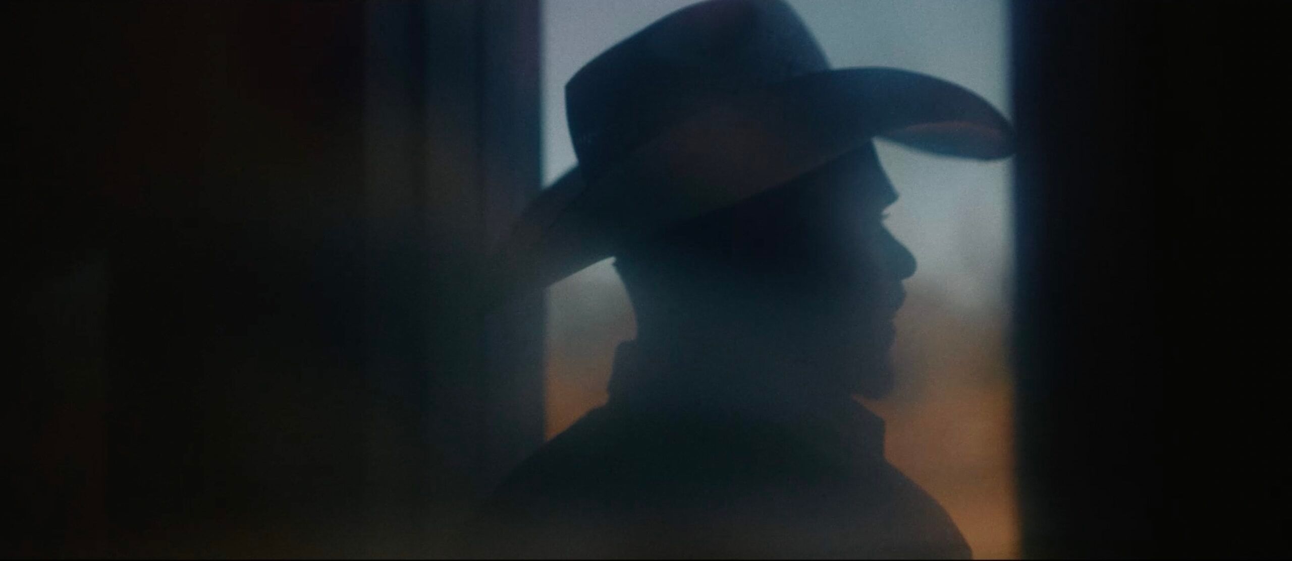 Silhouette of cowboy in hat against soft window light