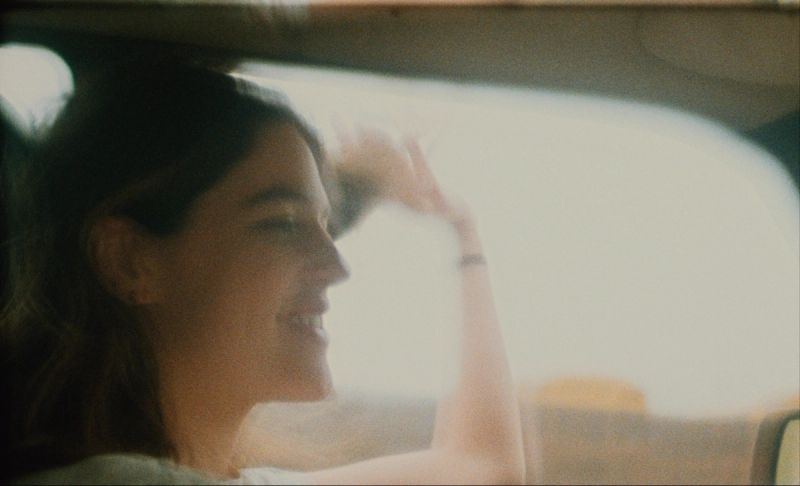 Woman smiling in car, hand shielding eyes from bright light