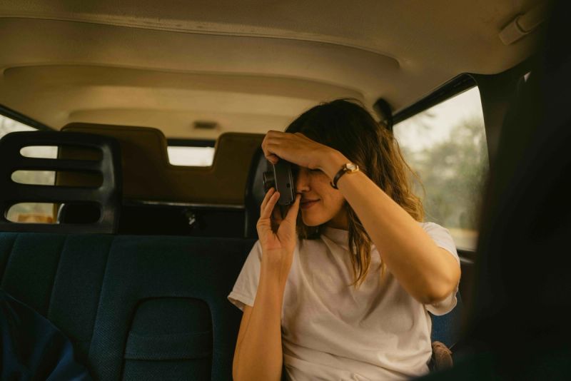 Woman in car holding camera to eye, adjusting lens with hand
