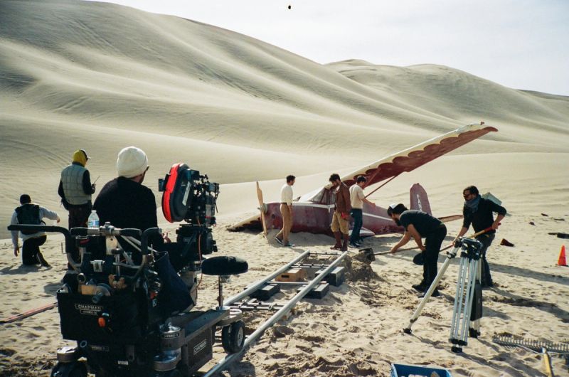Film crew on sand dunes with vintage plane during desert cinematography shoot