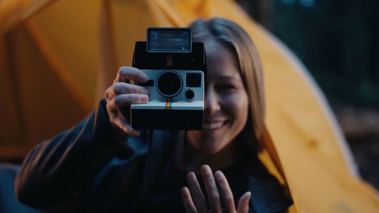 Smiling woman holding vintage Polaroid camera in front of yellow tent