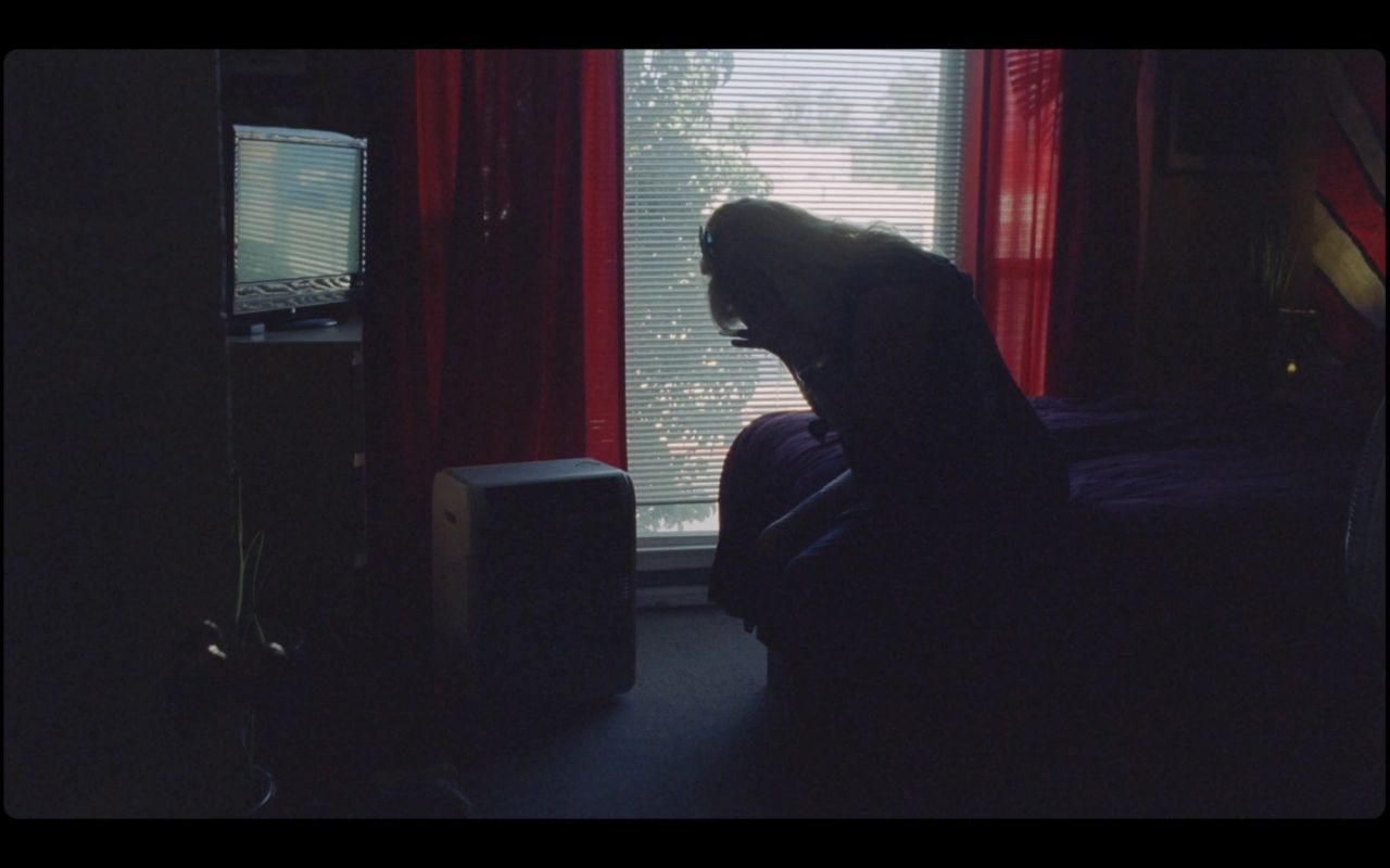 Silhouette of person sitting on bed in dimly lit room with window and red curtains