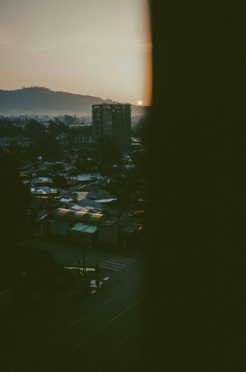 Sunset over an Ethiopian town with a building under construction and hazy mountains in the distance.