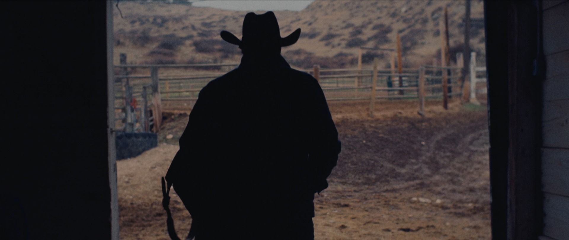 Silhouette of a cowboy in a hat walking toward a rural landscape