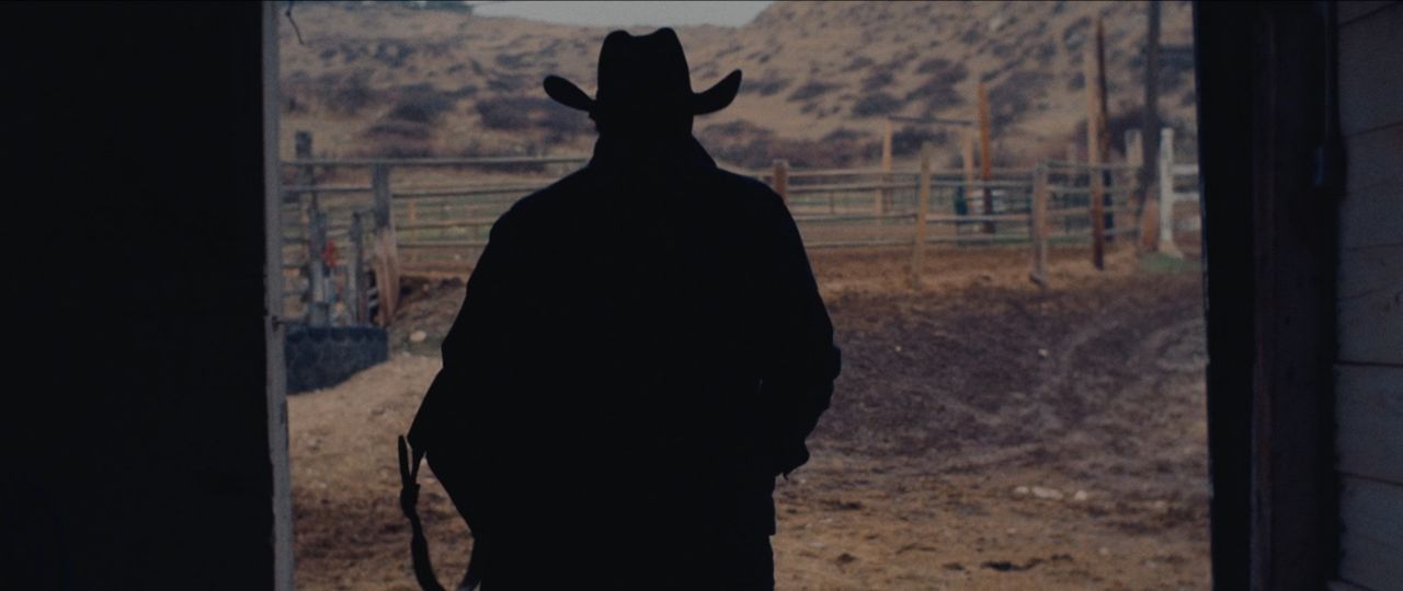 Silhouette of a cowboy in a hat walking toward a rural landscape