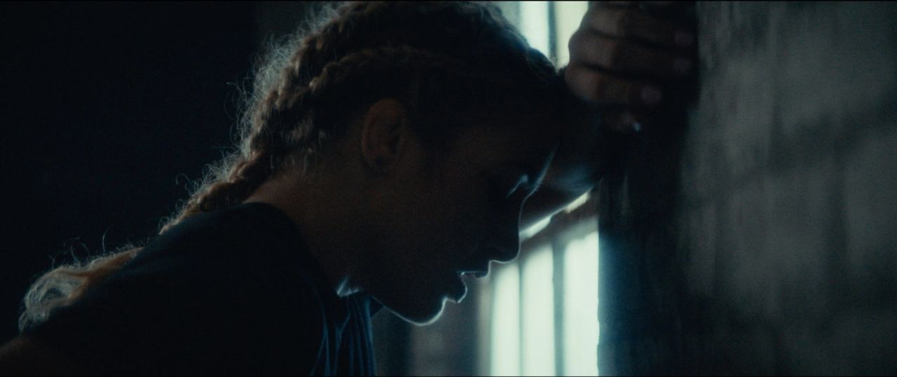 Profile of Olympic wrestler Helen Maroulis leaning against a wall, backlit by window bars in EastBay ConqHer.