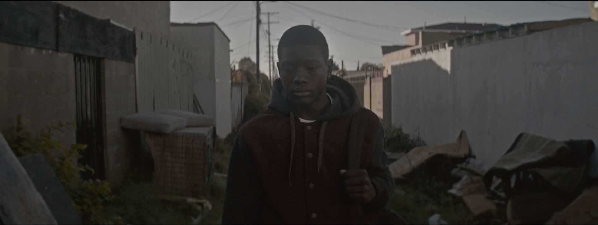 Young man in hoodie walking through narrow alleyway with buildings and debris