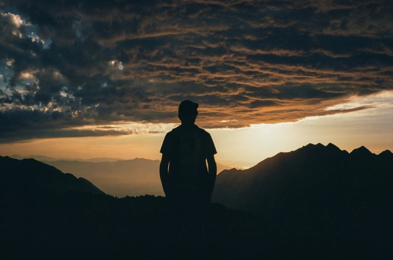 Silhouette of a figure standing on a mountain ridge against a dramatic sunset sky with clouds.