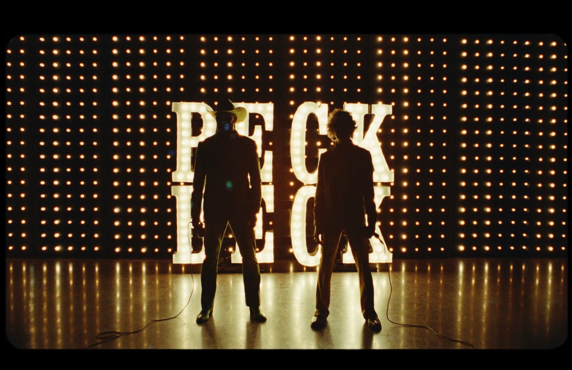 Orville Peck and Beck stand before illuminated 'PECK BECK' sign in Death Valley