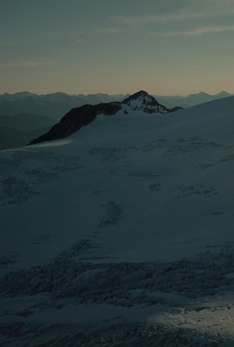 Snowy mountain ridge at dusk with distant peaks under soft sky