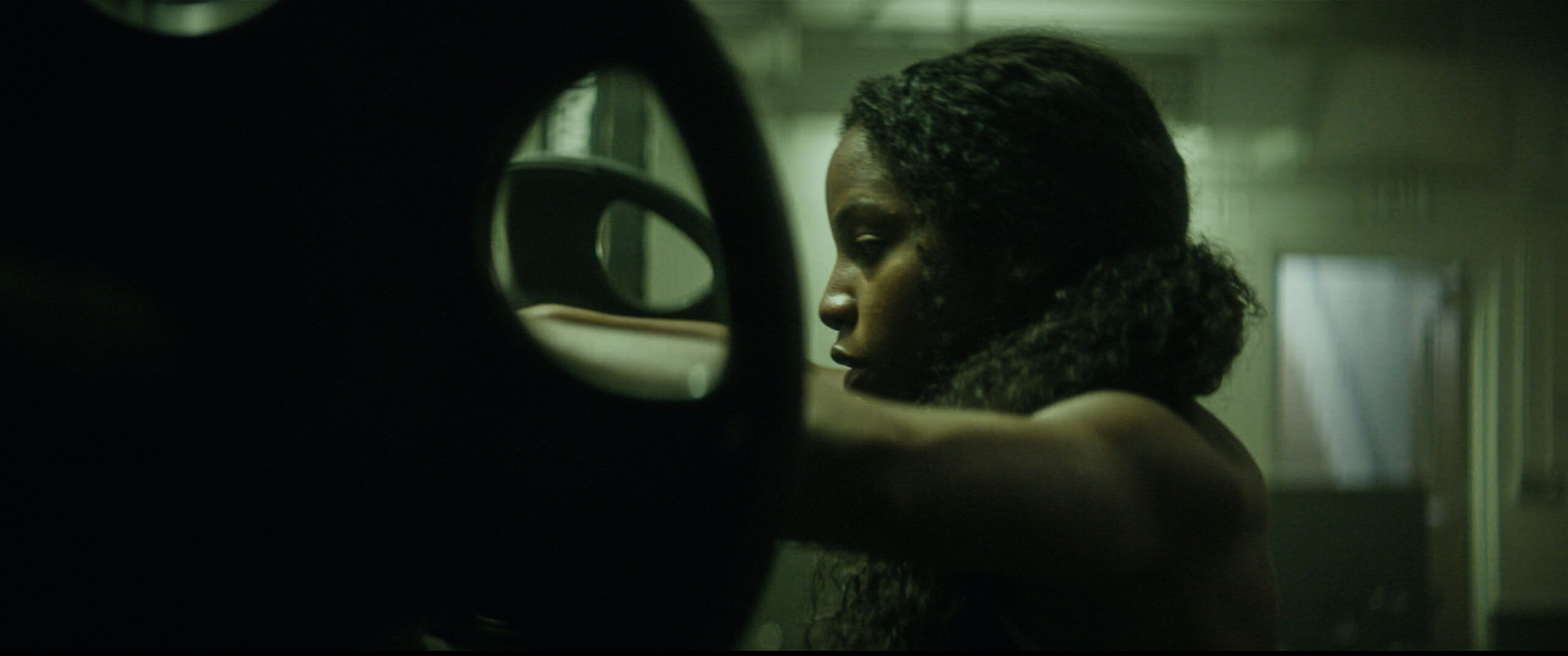 Profile of female athlete holding weight plate in dimly lit gym setting.