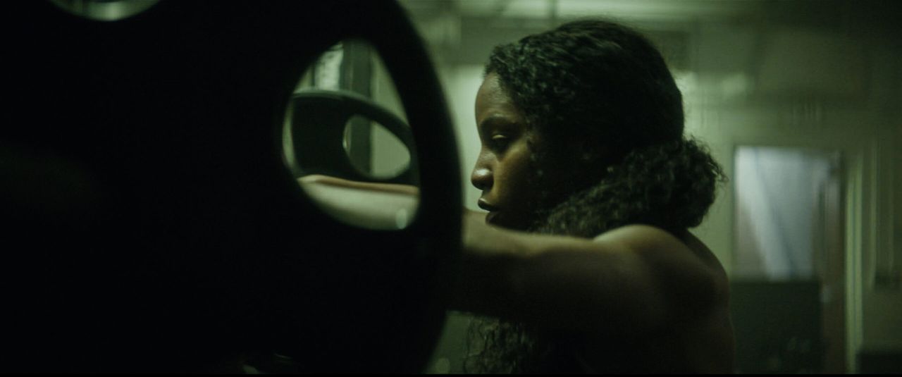 Profile of female athlete holding weight plate in dimly lit gym setting.