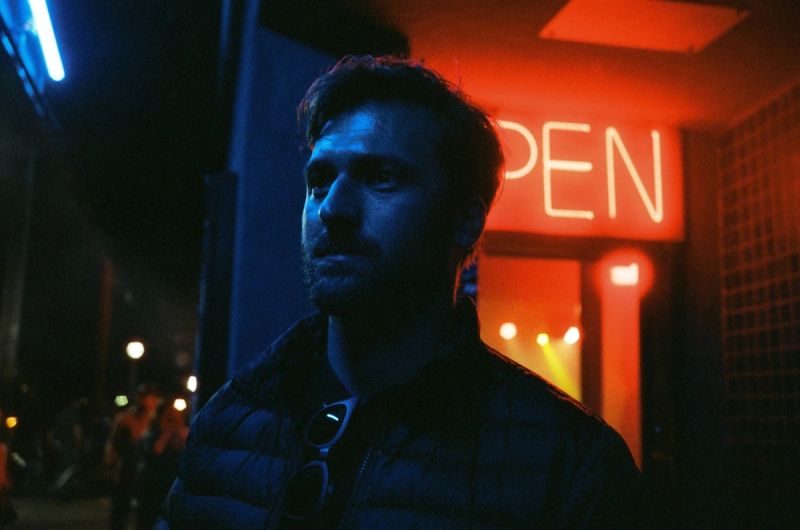 Man in puffer jacket under blue and red neon light at night