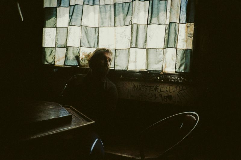 Director Trevor Paperny sits in a dimly lit room backlit by checkered curtains.