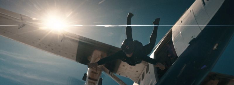 Skydiver in freefall exiting an aircraft against a bright sun with lens flare.
