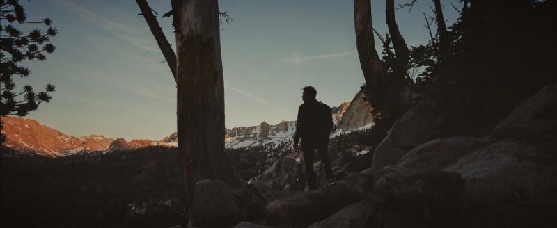 Silhouetted figure stands among trees overlooking snow-capped mountains, film photography at Mammoth Mountain.