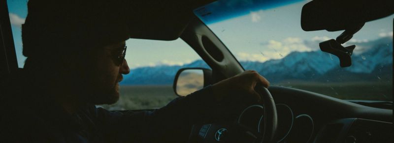 Cinematographer driving a Toyota vehicle with snow-capped mountains visible through the windshield.