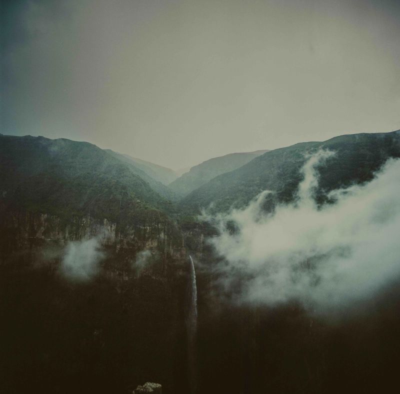Misty mountain valley with waterfall and clouds over rugged peaks